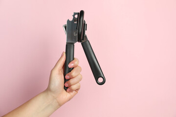 Woman holding can opener against pink background, closeup. Space for text