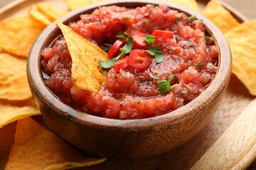 Delicious spicy salsa sauce in bowl and nacho chips on table, closeup