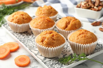 Tasty carrot muffins, cut vegetable and walnuts on white marble table, closeup