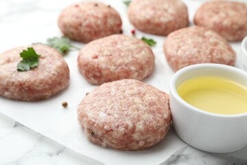 Many uncooked patties, oil and parsley on white table, closeup