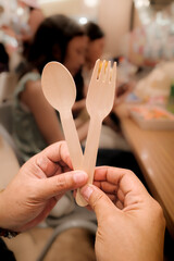 Closeup of disposable wooden cutlery with people eating at food court in the background
