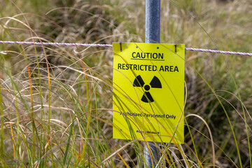 Caution restricted area radiation warning sign in a grassy outdoor environment indicating a hazardous zone