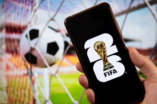 A male hand holding a smartphone with fifa world cup 2026 logo over a black background and a football goal blurred background