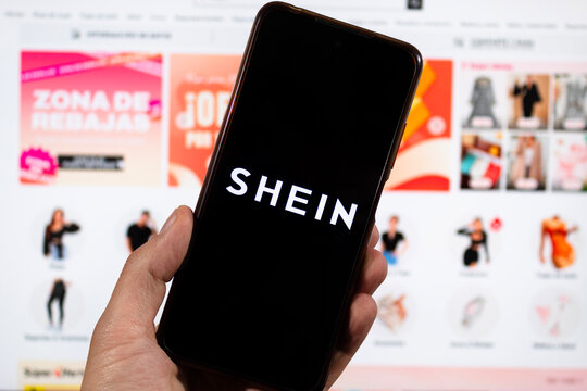 macro photo of a male hand holding a smartphone with his left hand and shein logo and blurred shein interface background