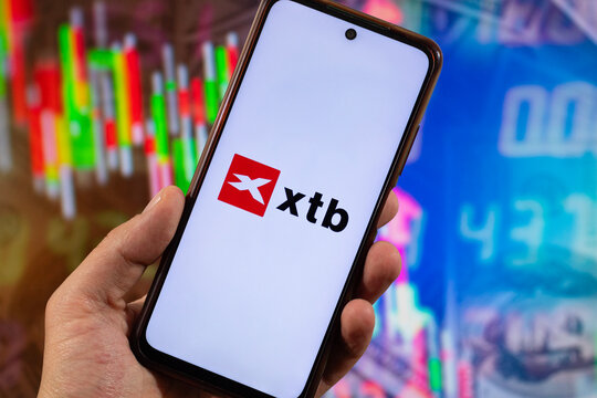 a smartphone with xtb stock exchange service logo and blurred finance concept at background