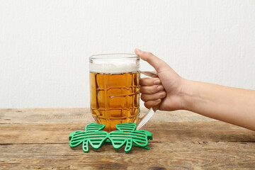 Female hand with mug of beer and plastic eyeglasses on wooden table against white background. St....