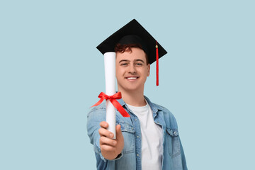 Male student in mortar board with diploma on blue background