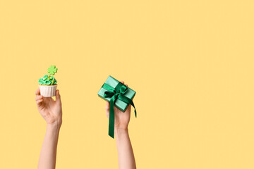 Female hands with tasty cupcake and gift box for St. Patrick's Day on beige background