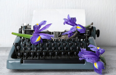 Vintage typewriter with paper sheet and purple flowers on grey grunge table near white wall