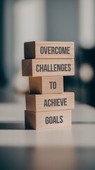 A stack of wooden blocks with "Overcome challenges to achieve goals" printed in dark brown letters. The blurred background shows a modern indoor space, emphasizing the motivational message.







