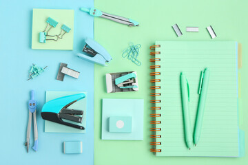 Staplers with different stationery supplies on color background