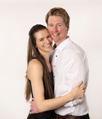 Attractive smiling young couple holding each other close isolated on light colored background