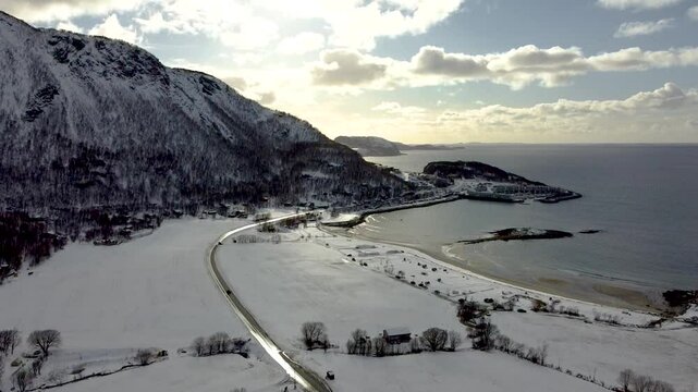 A breathtaking aerial view of pristine Arctic winter scenery, showcasing the majesteic highway of Northern Norway with snow covered beach and a stuning ocean in 4k.