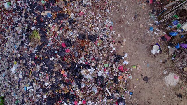 Aerial view of a landfill site filled with various types of waste, including plastic bags, food scraps, rotting fruits, and other discarded materials. Unleagual big garbage dump in Bali.