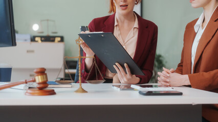 Two Caucasian women meet at a table, discussing legal matters. As lawyers, they advise clients on...