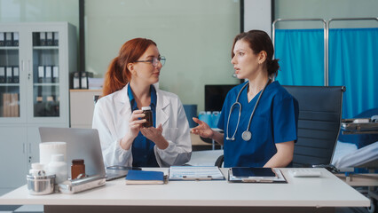 Two Caucasian female doctors work at a desk, meeting and discussing patient treatment while using a medical program modern technology in a hospital to ensure effective healthcare medicine management