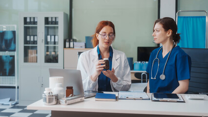 Two Caucasian female doctors work at a desk, meeting and discussing patient treatment while using a medical program modern technology in a hospital to ensure effective healthcare medicine management