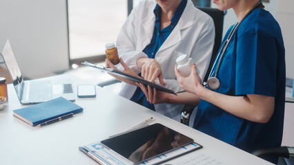 Two Caucasian female doctors work at a desk, meeting and discussing patient treatment while using a...