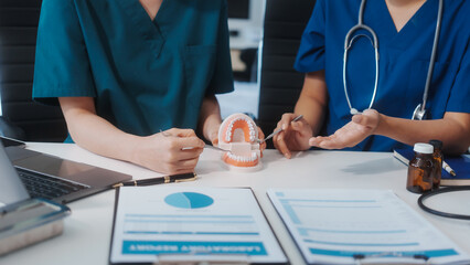 Two Asian female doctors meet at a table in a clinic, with a dentist explaining dental...