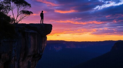 Fototapeta premium man silhouette at cliff edge sunset over valley