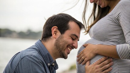 A joyful couple embraces the anticipation of parenthood, with the partner smiling at the pregnant belly against a serene outdoor backdrop.