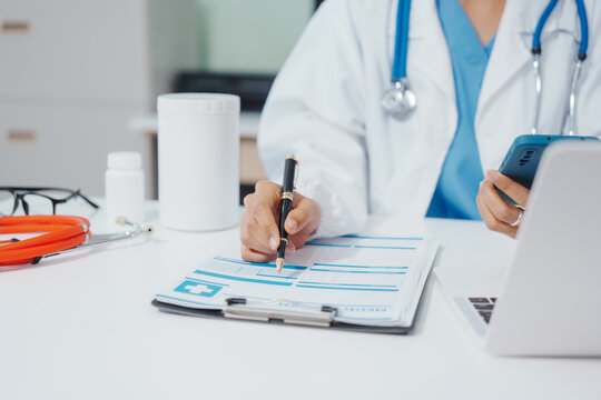 Asian female doctor is reviewing medical records, working on a computer, planning treatment, giving online consultations, and explaining medications to patients via a medical video call in a clinic