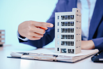 A female employee works at her desk in a real estate office, managing condo sales in the city. She...