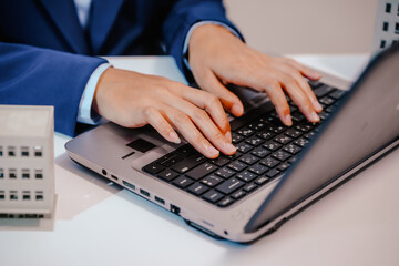 A female employee works at her desk in a real estate office, managing condo sales in the city. She...