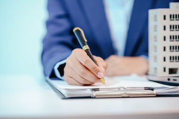 A female employee works at her desk in a real estate office, managing condo sales in the city. She...