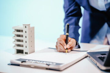 A female employee works at her desk in a real estate office, managing condo sales in the city. She...