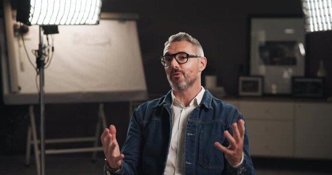 Talking, interview and man on set with camera for filming with documentary, show or movie in studio. Record, discussion and journalist by lights for TV public speaking with production equipment.