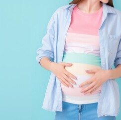 Pregnant woman in casual attire with hands on her belly against a blue background.