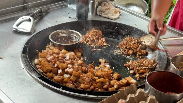 A close-up of a vendor making fried carrot cake in a wok on a hawker street food stall in Penang, Malaysia