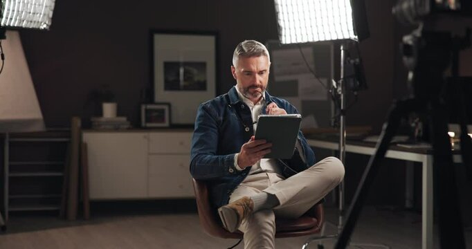 Tablet, filming and man on set reading script for documentary interview or podcast episode. Digital technology, research and male journalist recording for online live streaming show with lights.