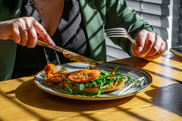 woman eating burger with fork and knife in restaurant. burger with arugula, chicken cutlet, tomato.