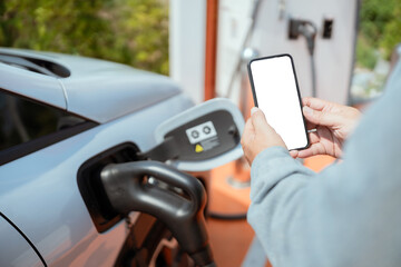 Driver using smartphone at electric vehicle charging station during early morning