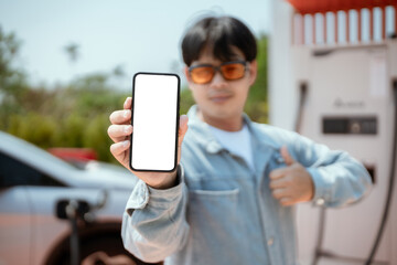 Man showcasing smartphone at electric vehicle charging station in a sunny outdoor setting