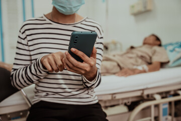 A daughter sits by her elderly father's hospital bedside, caring for him, giving him medicine, holding his hand and encouraging him as he struggles with the stress of his treatment and medical bills