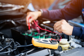 A mechanic is working on a car engine. He uses a multimeter to check the battery.