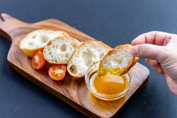 木製ボードに並ぶ、黄金色のオリーブオイルを添えた香ばしいバゲット。外はカリッと中はふんわりとしたパンの質感と、オイルの艶やかな光沢が食欲をそそる。ワインの供やイタリアン・バルの軽食、パーティーの素材として最適な、シンプルで洗練された俯瞰カット。 | Sliced baguette with golden olive oil on a wooden board.