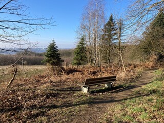 Landschaft in der Natur im Winter / Frühling mit Bank und Blick über Wald und Felder, Richtung...