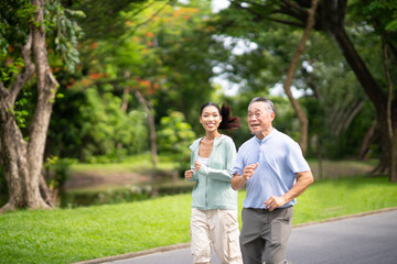 Fototapeta premium Young beautiful Asian woman jogging with her father in summer park with a smile. Healthy woman and senior man do exercise for health, health care, life insurance concept.