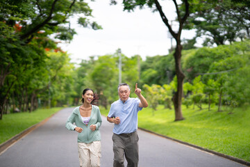Fototapeta premium Young Asian woman jogging with her father in summer park with smile. Healthy woman and senior man do exercise for health, lady and olderry man workout together, health care, life insurance concept.