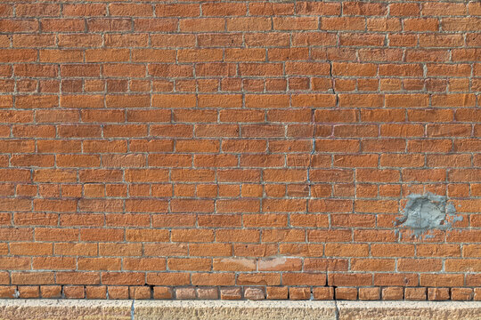 Abstract texture background of a weathered exterior vintage orange color brick wall surface, with beige limestone foundation at bottom