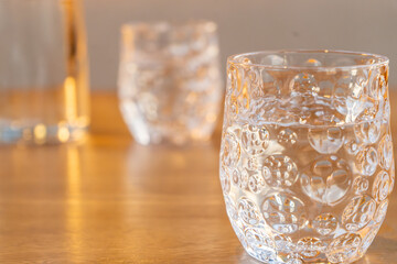 A beautifully designed water glass with a unique bubble texture sits on a wooden table, filled with clear water. The soft lighting enhances the transparency and reflections, adding depth and elegance 