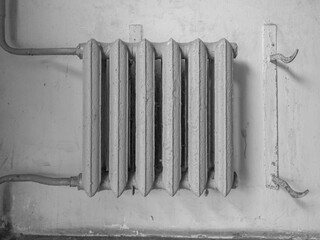An old, cast iron radiator is hanged on old dirty gray wall. The radiator has a weathered, gray...