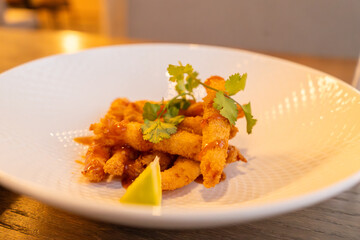 A beautifully presented crispy fried appetizer garnished with fresh cilantro and drizzled with a savory sauce. The dish is served on a white plate, accompanied by a wedge of lemon for added zest. 