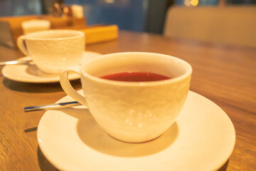 A close-up of two white porcelain tea cups filled with tea, placed on matching saucers on a wooden table. The soft ambient lighting enhances the inviting atmosphere, making this a perfect setting