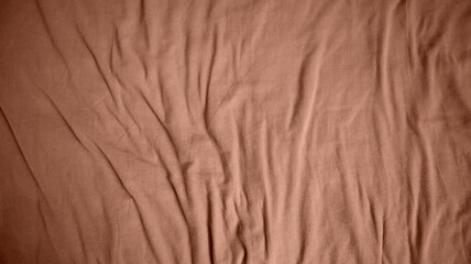 Photo of a fabric background. Uneven folds. More folds at the bottom of the background. Different shades. Mocha Mousse color. Color of the year 2025.