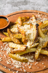 Parmesan wedge fries with sauce on a cutting board